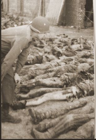 An American soldier examines the corpses of prisoners killed by the SS in a barn.jpg